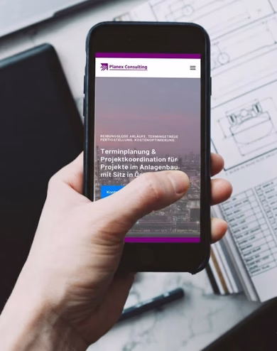 Eine Hand hält ein Smartphone mit der mobilen Website von Planex Consulting, im Hintergrund liegen technische Zeichnungen und Baupläne auf einem Schreibtisch.