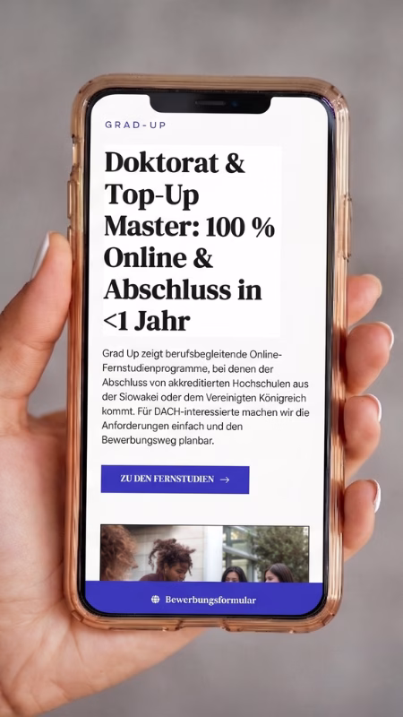 Eine Hand hält ein Smartphone, das die mobile Ansicht der neu gestalteten Grad-Up Website mit dem Titel „Doktorat & Top-Up Master: 100 % Online“ zeigt.