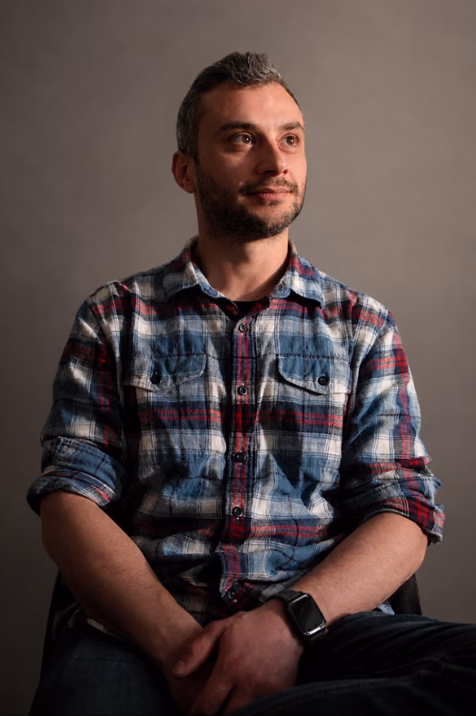 Porträt von Stefan, SEO-Experte und Kfz-Technik-Meister, in einem karierten Hemd blickt zuversichtlich zur Seite vor grauem Hintergrund.